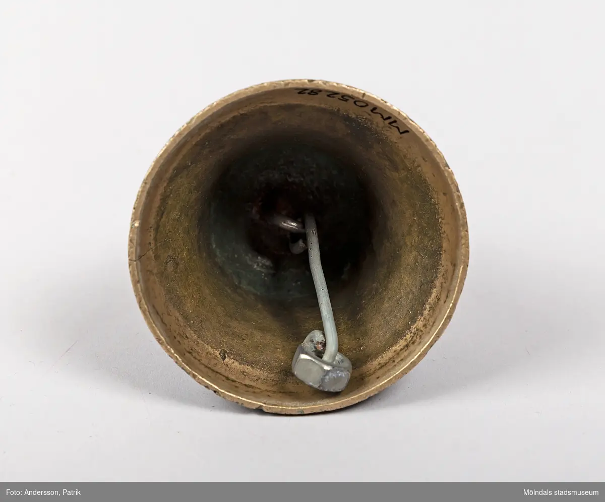 Liten klocka med kläpp av metall. Kläppen har vid något tillfälle gått sönder och ersatts med en bit ståltråd och en mutter. Klockan är 8 cm hög och har diameter på 8,5 cm. Klockan har använts för att ringa in till maten vid Gåreviks Barnkoloni.