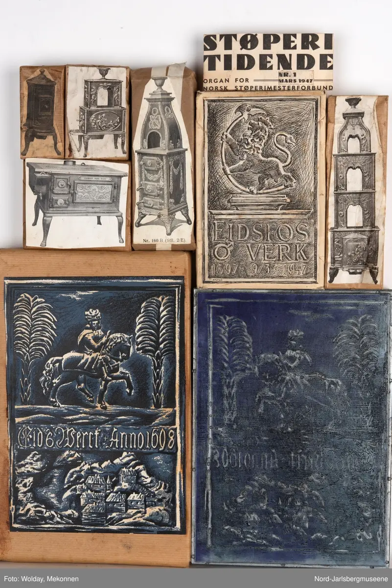 Klisjjer pakket inn i papir med motivbildet pålimt oppå motivene er diverse ovnsmodeller og illustrasjoner til Eidsfos Verks jubileumsskrift 1897.