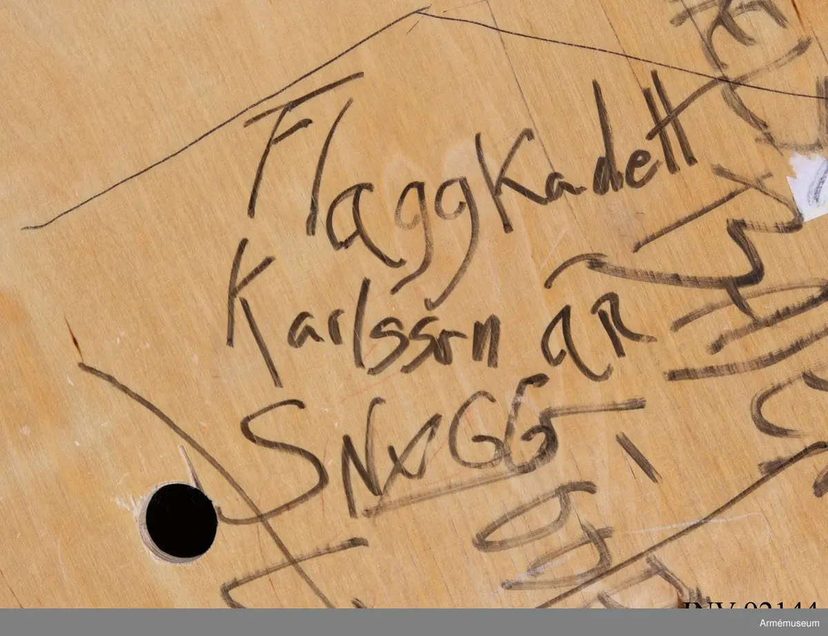 Sängbotten i trä avsedd för våningssäng i metall. Nedklottrad med text och bilder av mestadels sexistisk karaktär. Flertalet kommentarer berör muck och skilda idrottslag.