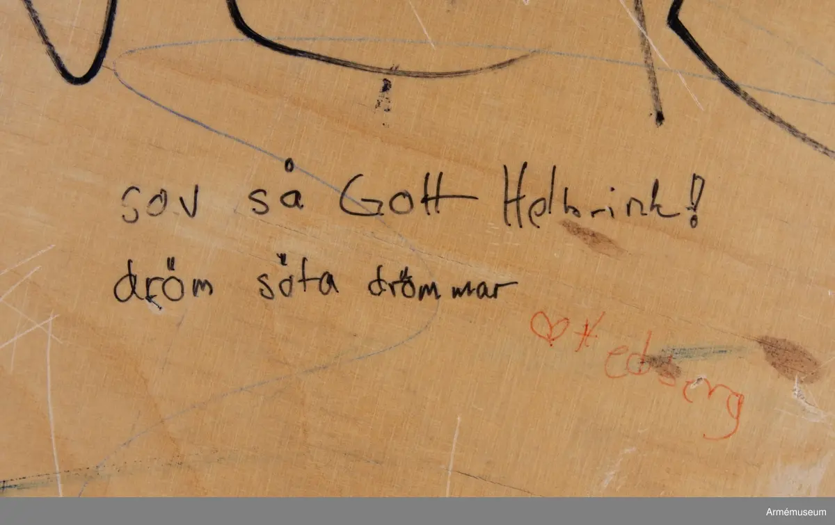 Sängbotten i trä avsedd för våningssäng i metall. Nedklottrad med text och bilder av mestadels sexistisk karaktär. Flertalet kommentarer berör muck och värnpliktens vardag i övrigt. En klisterlapp med Sjöfartsverkets tio sjövettsregler, liksom fem mindre klisterlappar från snusdosor av märkena Göteborgs rapé och General är fastsatta.