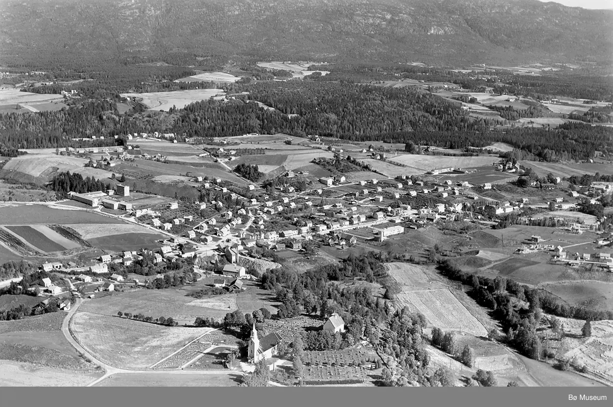 Flyfoto av Bøhaugen med kyrkjene og Midt-Bø gardane, tatt 5. juli 1952.