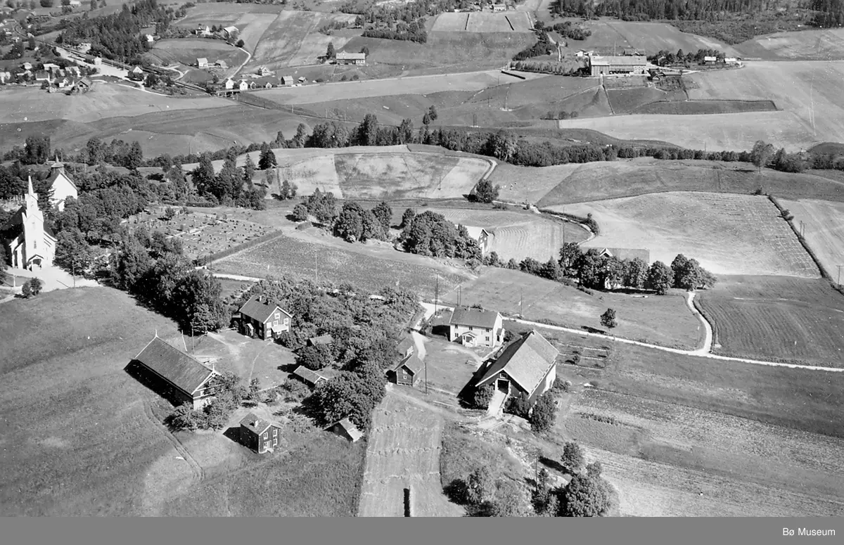 Flyfoto av Bøhaugen med kyrkjene og Midt-Bø gardane, tatt 5. juli 1952.