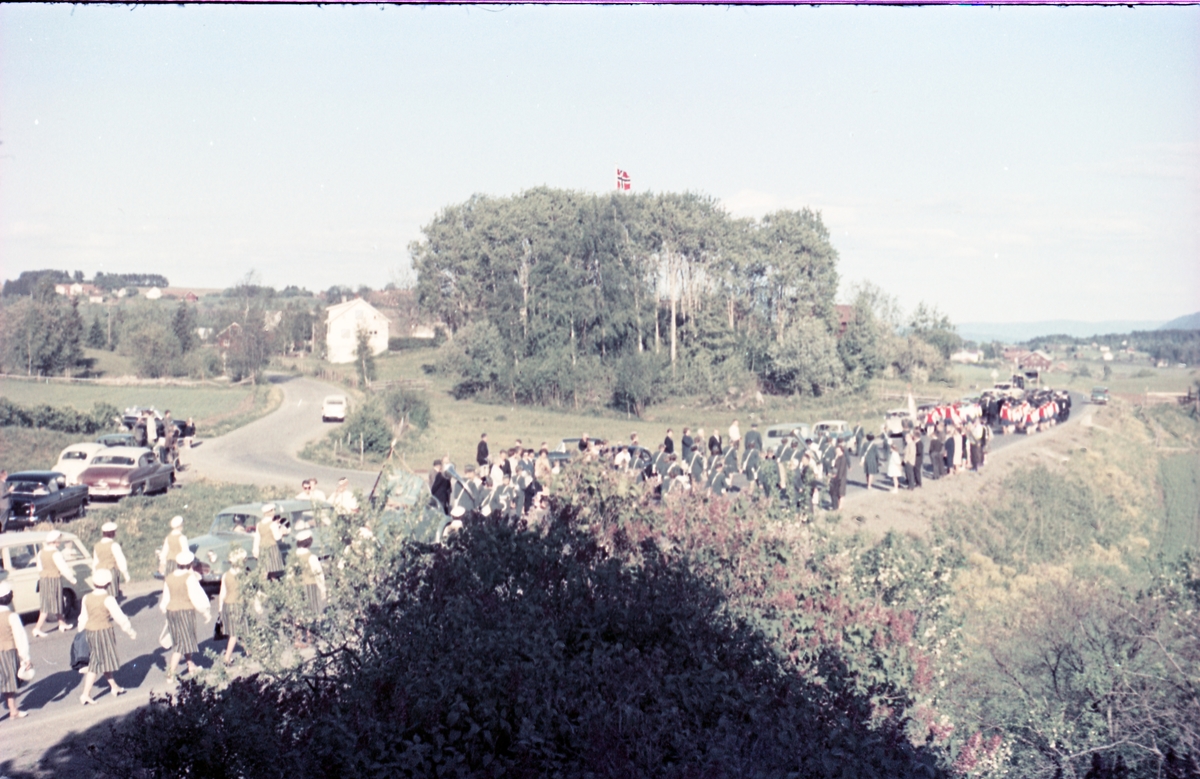 Serie på 16 bilder trolig fra Sangens og Musikkens Dag i Østre Toten, muligens 1961. Bildene er tatt i retning Brunsberg fra fotografens eiendom Odberg på Kraby, der forskjellige korps og kor deffilerer forbi.
