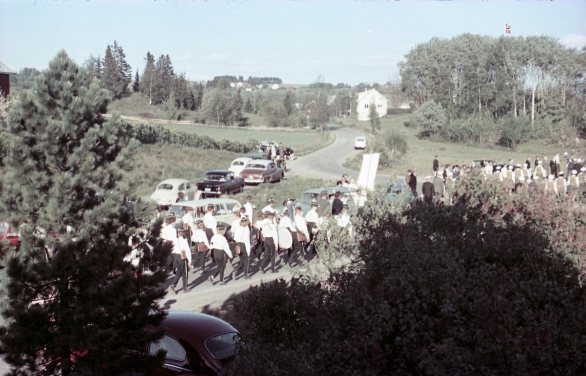Serie på 16 bilder trolig fra Sangens og Musikkens Dag i Østre Toten, muligens 1961. Bildene er tatt i retning Brunsberg fra fotografens eiendom Odberg på Kraby, der forskjellige korps og kor deffilerer forbi.