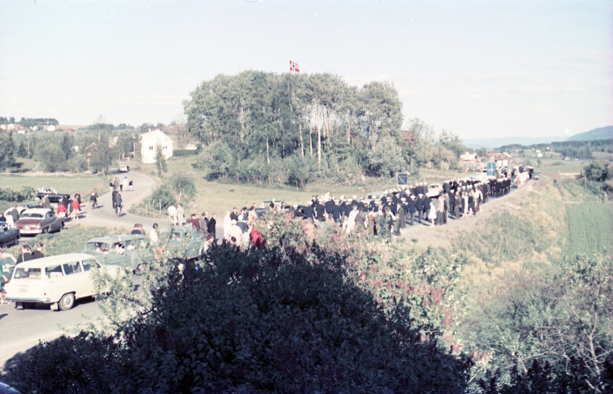 Serie på 16 bilder trolig fra Sangens og Musikkens Dag i Østre Toten, muligens 1961. Bildene er tatt i retning Brunsberg fra fotografens eiendom Odberg på Kraby, der forskjellige korps og kor deffilerer forbi.