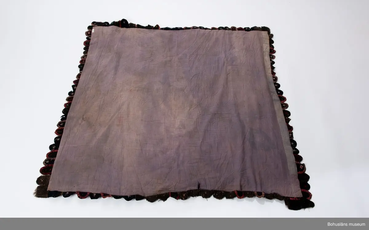 Tillverkningstid: Troligen 1900-talets början.
Användningstid: Troligen 1900-talets första hälft.

Stickad botten av bomullsmattvarp (oblekt), kulörta ylle-, linne-, och bomullstrasor inlagda alternativt insatta i bottenmaterialet [ej nedsydda] . (Man kan antingen välja mellan att lägga in trasor medan man stickar alternativt sätta in dem i den färdiga botten.) 
Runtom i två lager, halvsfäriskt formade yllelappar av olika kvaliteter, påsydda, överlappande varandra. Lapparna langetterade runtom, broderat blommotiv i mitten av varje lapp, liknande de klackmattor som helt och hållet täcktes av klackformade lappar.
Mattan fodrad med ett blågrått bomullstyg. 
Nött, skador av användning, en bristning i fodret.

Se bilagepärm UM022278: Beskrivningar ur IDUN nr. 50/1889; John Hinchcliffe, Angela Jeffs, Trasmattor, Forum 1978.

Litteratur: Kerstin Ankert/Ingrid Frankow. Den svenska trasmattan - en kulturhistoria, Prisma 2003.