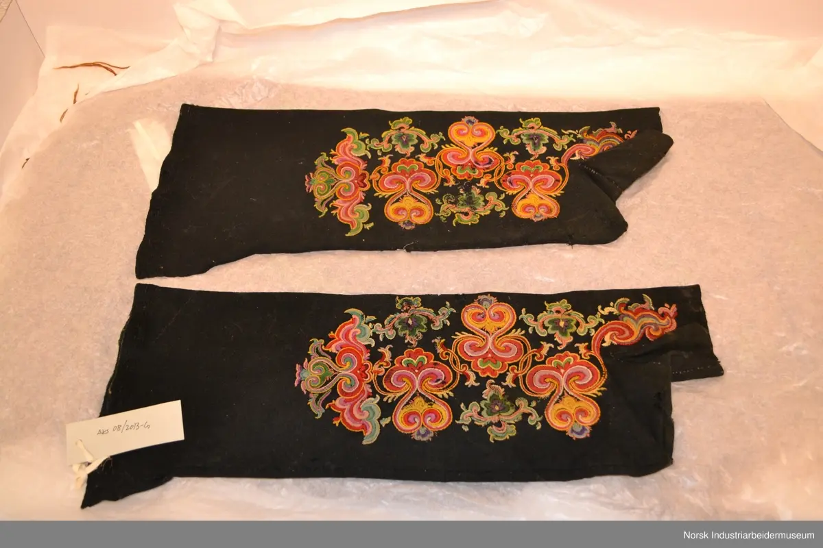 Sokkene er sydd av svart vadmel med rosesøm, brodert mønster i farget ullgarn, typisk for Øst-Telemark. Fargene som er brukt: Gult, orange, lys og mørk grønn, rosa, lys blå, burgunder og lilla. Sokkene er slitt med en del hull og skader på broderiet. Broderigarnets farger er fortsatt sterke. Hver sokk er brodert på to sider. Det er det samme mønsteret som repeteres. 
Sokkene går til knærne. De mangler tå.
