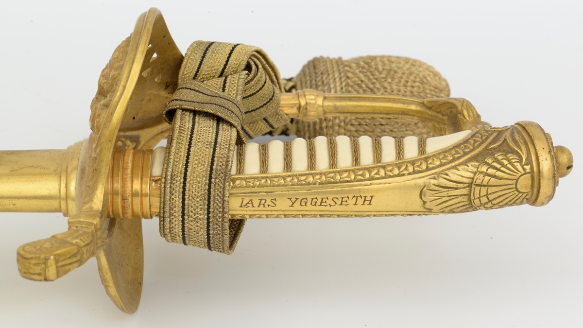 Norsk marinesabel Modell 1842. Feste i forgyllyt messing. Flat knapp med blomstermotiv. Nakkestykke merket "Lars Yggeseth"
Hvitt plastgrep med riller med snodd messingtråd i rillene. Gjennombrutt parerplate på utsiden med urent anker..Bakre parerstang svakt medbøyd og ender i en flattykt kule. Fremre parerstang går over i håndbøylen.
Gulltråde portepé flettet med alternativt svart/mørkeblått og gull.
Svakt krummet enegget klinge med rygg- og midtstillt blodrand. Klingen har etset dekor med moderne marinefartøy og kronet urent anker. Klimgen er merket med Carl Eichorns Solingenstempep i en oval rundt et ekorn.
Lærbalg med forgyllte messingbeslag. Munnblikket merket med norsk løve på forsiden og " Y " på baksiden. Midtbåndet er merket med kronet urent anker. Doppskoen har Neptuns tref ork og militære attributter.