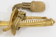 Norsk marinesabel Modell 1842. Feste i forgyllyt messing. Flat knapp med blomstermotiv. Nakkestykke merket "Lars Yggeseth"
Hvitt plastgrep med riller med snodd messingtråd i rillene. Gjennombrutt parerplate på utsiden med urent anker..Bakre parerstang svakt medbøyd og ender i en flattykt kule. Fremre parerstang går over i håndbøylen.
Gulltråde portepé flettet med alternativt svart/mørkeblått og gull.
Svakt krummet enegget klinge med rygg- og midtstillt blodrand. Klingen har etset dekor med moderne marinefartøy og kronet urent anker. Klimgen er merket med Carl Eichorns Solingenstempep i en oval rundt et ekorn.
Lærbalg med forgyllte messingbeslag. Munnblikket merket med norsk løve på forsiden og " Y " på baksiden. Midtbåndet er merket med kronet urent anker. Doppskoen har Neptuns tref ork og militære attributter.