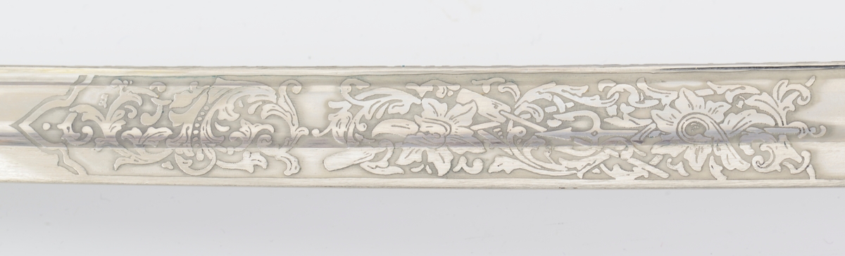 Norsk marinesabel Modell 1842. Feste i forgyllyt messing. Flat knapp med blomstermotiv. Nakkestykke merket "Lars Yggeseth"
Hvitt plastgrep med riller med snodd messingtråd i rillene. Gjennombrutt parerplate på utsiden med urent anker..Bakre parerstang svakt medbøyd og ender i en flattykt kule. Fremre parerstang går over i håndbøylen.
Gulltråde portepé flettet med alternativt svart/mørkeblått og gull.
Svakt krummet enegget klinge med rygg- og midtstillt blodrand. Klingen har etset dekor med moderne marinefartøy og kronet urent anker. Klimgen er merket med Carl Eichorns Solingenstempep i en oval rundt et ekorn.
Lærbalg med forgyllte messingbeslag. Munnblikket merket med norsk løve på forsiden og " Y " på baksiden. Midtbåndet er merket med kronet urent anker. Doppskoen har Neptuns tref ork og militære attributter.