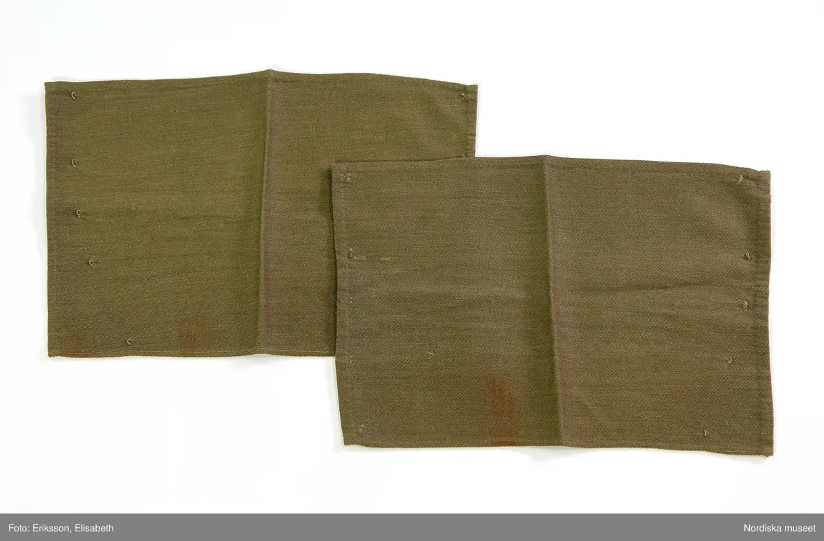 Ett par damasker av grönbrun yllediagonal, nära rektangulära men något avsmalnande. Höjd ca 25 cm, största bredd ca 38 cm. Knäpps ihop med fem hakar och sydda hyskor.

På båda damaskerna, enstaka skador i tyget och rödtonade fläckar.

/Marianne Larsson 2019-03-01