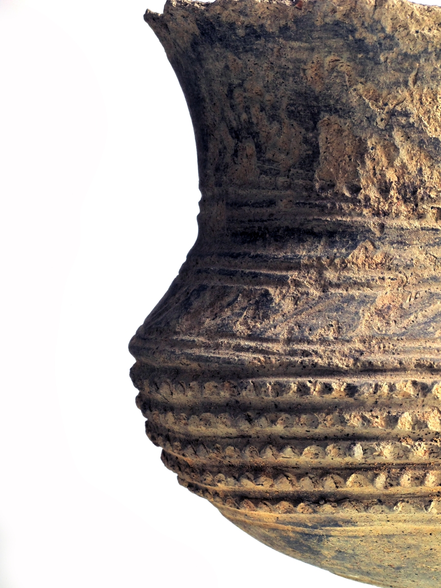 Vorte-kar med hank av lyst grålig, temmelig tynt gods av form nærmest som Bøe: anf. arb., fig. 136. Hals- og skulderornering består øverst og nederst av tre dobbelte linjebunter; over disse en punktert linje, mellom dem en hulkile og endelig parvis skråstilte linjer. Orneringen bøyer ned på begge sider av hanken. På øvre del av buken 5 rekker med vorter av samme type som anf. arb. fig. 135, men mer tettstilte. Nedre del uornert. Bunnen, som er oppdrevet, er avgrenset med en dobbeltlinje. Noen skår mangler ved randen,hanken er avslått og overflaten noe avskallet, ellers bra bevart.