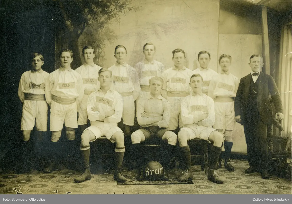 "Brann" fotballklub i Sarpsborg, gruppeportrett.  Bl.a. Asbjørn Nilsen, klubbens formann i mange år. Ifølge opplysninger stiftet i 1916, men opplyst at bildet tatt ca. 1914(?) Da klubben ble oppløst fordelte medlemmene seg på andre lag, f.eks. Sarpsborg Fotballklubb. Senere kom et fotballag i Sarpsborg med samme navn tilsluttet Arbeidernes Idrettsforbund.