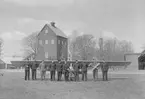 Porträttfotografi av militärer och civilklädda män framför ett glidflygplan på flygfältet på F 3 Malmen, 1942. I bakgrunden syns vattentornet på F 3 Malmen. En av männen håller ett modellflygplan.