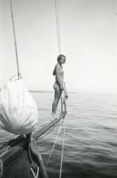 Ung kvinna i baddräkt poserar på bogsprötet.