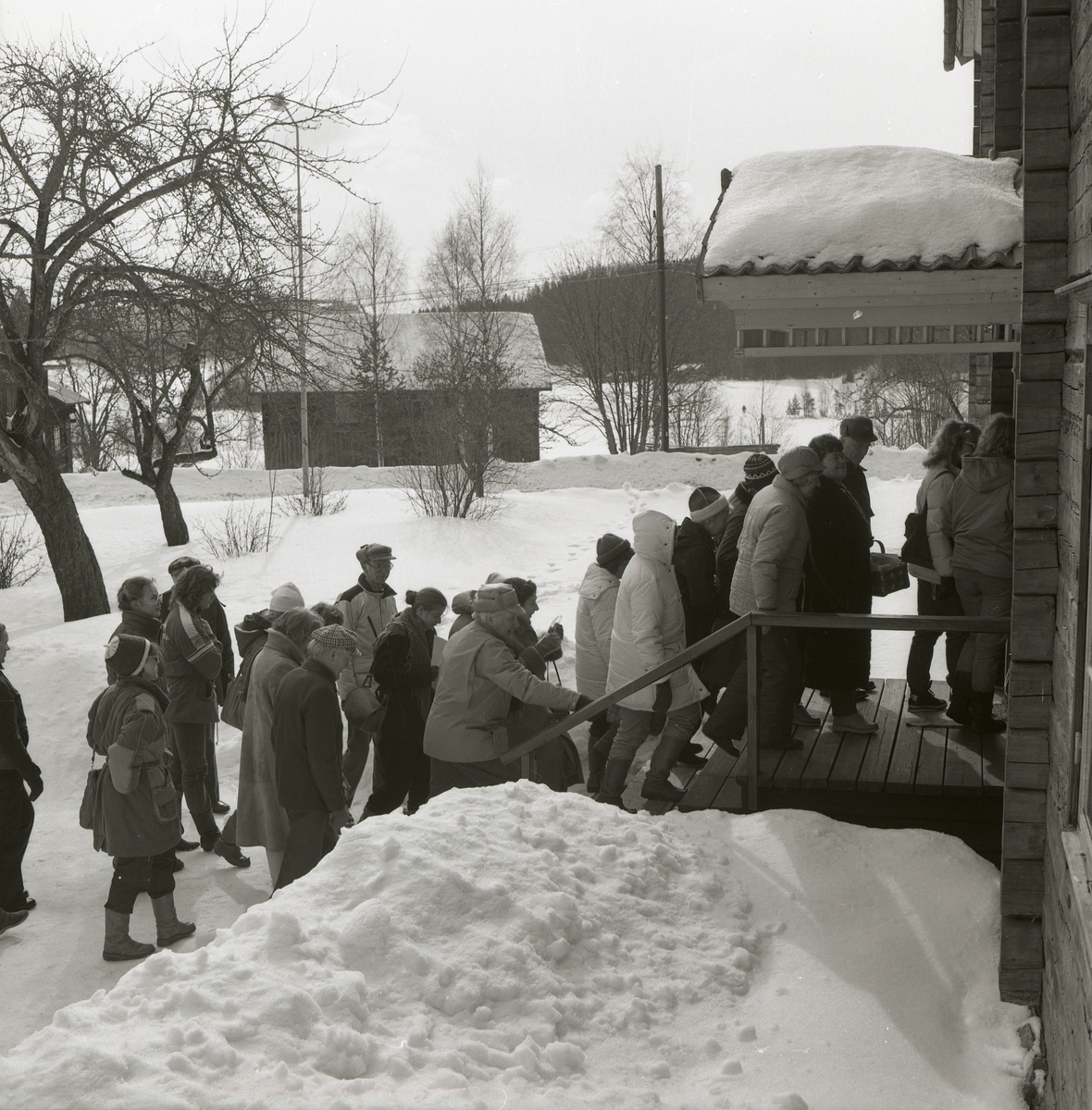 En folksamling går in i en byggnad för att delta i en hembygdskurs vid Hembygdsbyn i Rengsjö, 1984.