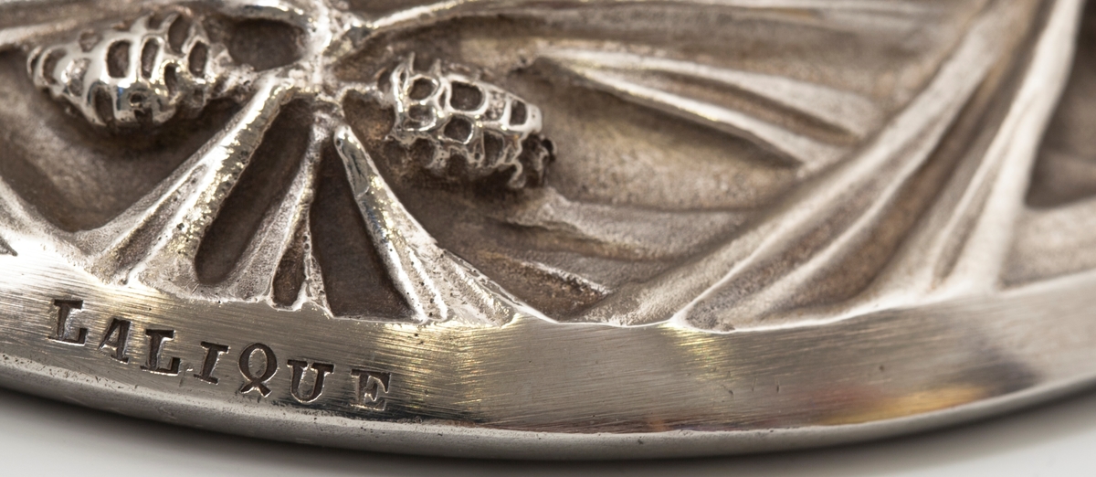 Pokal utført i støpt sølv og halvgjennomskinnelig melkehvitt opalinglass. Det gjennombrutte sølvet danner et flettverk av pinjekongler, grener og nåler i relieff, som brer seg fra den halvkuleformede kupaen og nedover den koniske stetten. Overgangen mellom disse to delene er markert med en ringformet vulst. Inne i pokalen er det innblåst opalinglass, som delvis trer frem som glassblærer på dens ytterside. På foten er det rektangulære felter med stiliserte kongler og grener i lavt relieff.