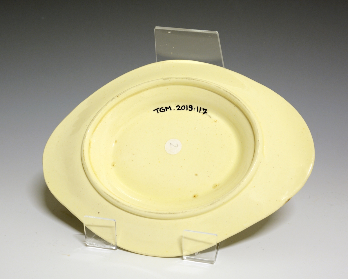 Sauseterrin med lokk og løst underfat. Høy lokknapp og høyreiste hanker i hver side. Sort dekor of sorte kantrender. MOnogrammet "NU" både på lokket og korpus.
