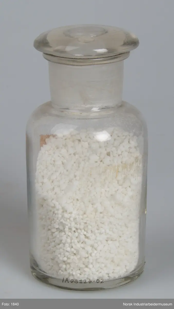 Laboratorieglas med prøve af den første produktion af kalksalpeter.
Cylindrisk laboratorieglas med slebet glasprop. Indeholder salpeter i form af små hvide perler og gryn.