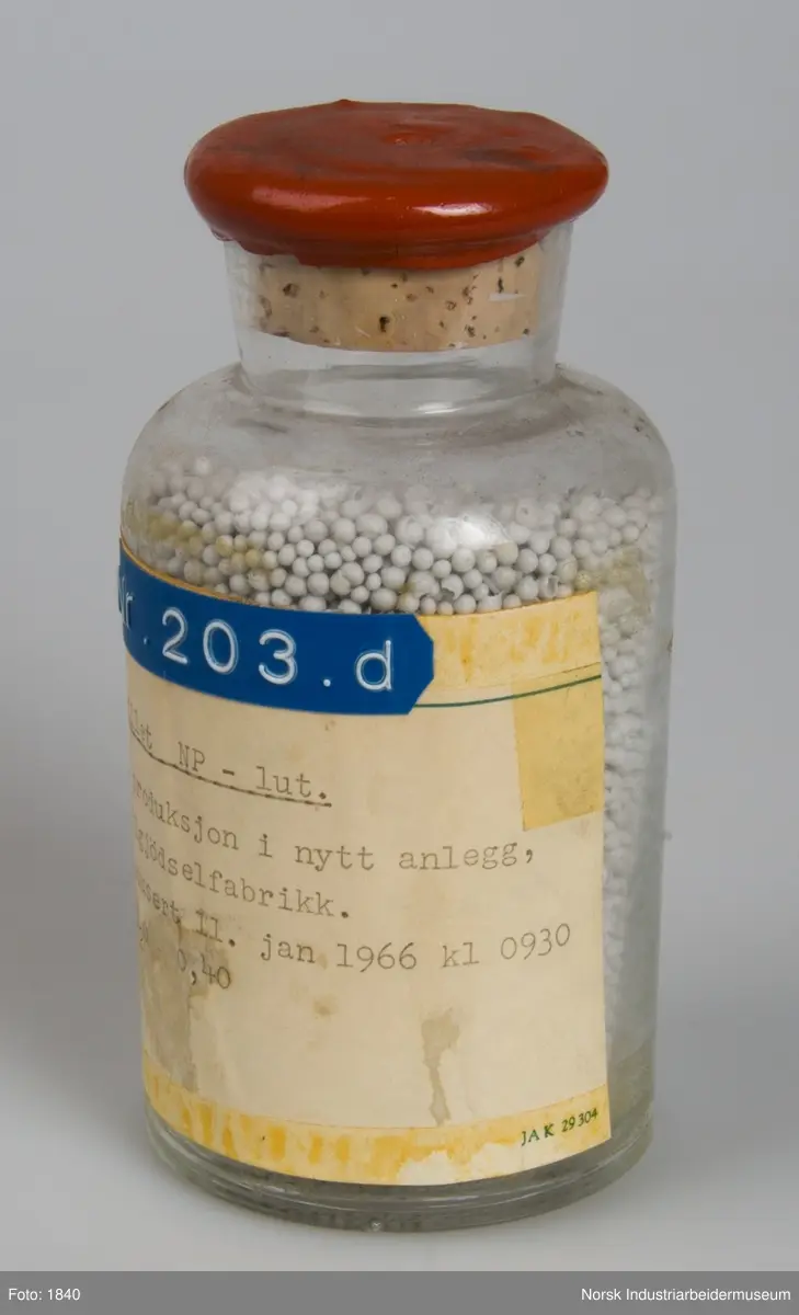 Cylindrisk laboratorieglas med lakforseglet korkprop der indeholder prillet NP - lut.