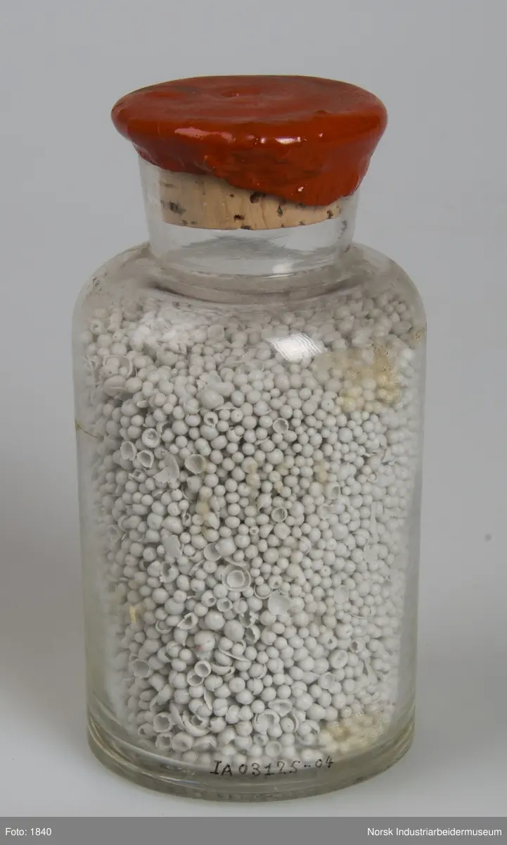 Cylindrisk laboratorieglas med lakforseglet korkprop der indeholder prillet NP - lut.