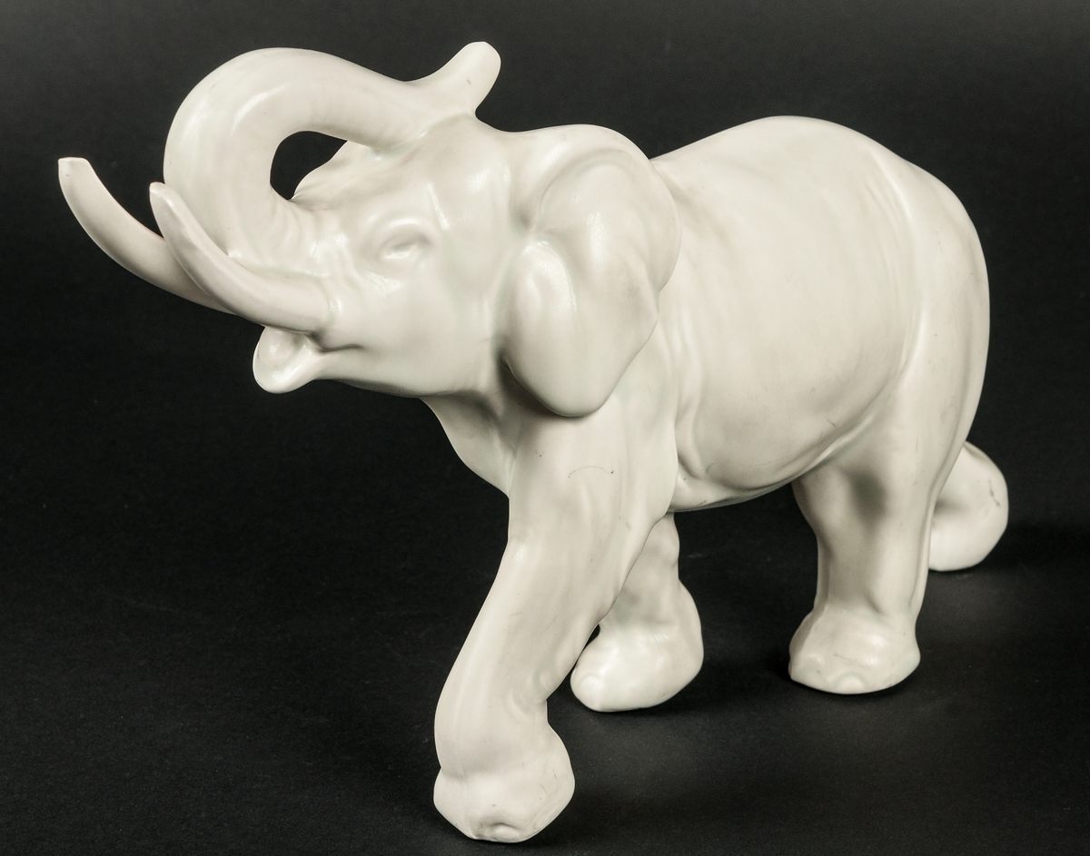 Elefant i keramik, med höjd snabet. Gråvit matt glasyr.