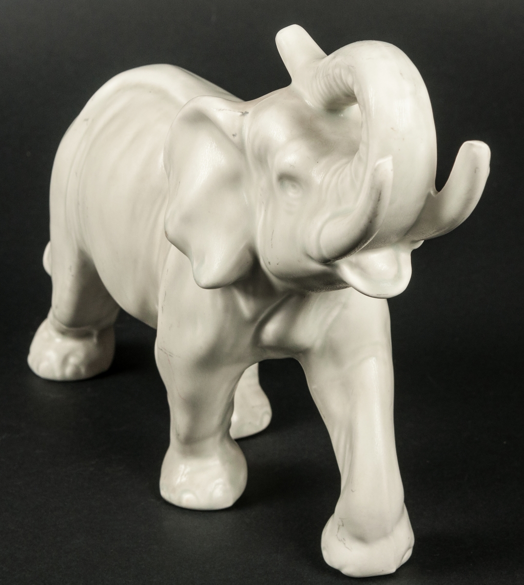 Elefant i keramik, med höjd snabet. Gråvit matt glasyr.