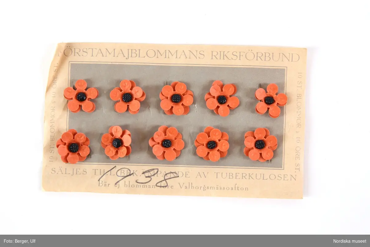 Majblomskarta med 1936 års eller 1938 års majblommor.
Ljusgrå  karta med beige ram, av rektangulärt papper med tryckt text  i ljusgråttlt: "FÖRSTAMAJBLOMMANS RIKSFÖRBUND. SÄLJES TILL BEKÄMPANDE AV TUBERKULOSEN. Bär ej blomman före Valborgsmässoafton.10 ST. BLOMMOR à 10 ÖRE ST." Handskriven sekundär påskift i blyerts på framsidan av kartan "1938". På kartan fästa 10 st majblommor av papper  med dubbla kronblad i orange med svart mittknopp av glas och nål av gulmetall.
På baksidan ingen tryckt text.
Lena Kättström Höök/ 2013-04-23

Vid försäljningen var majblommorna fästade på detta sätt.
/Lena Kättström Höök 2008-11-17
