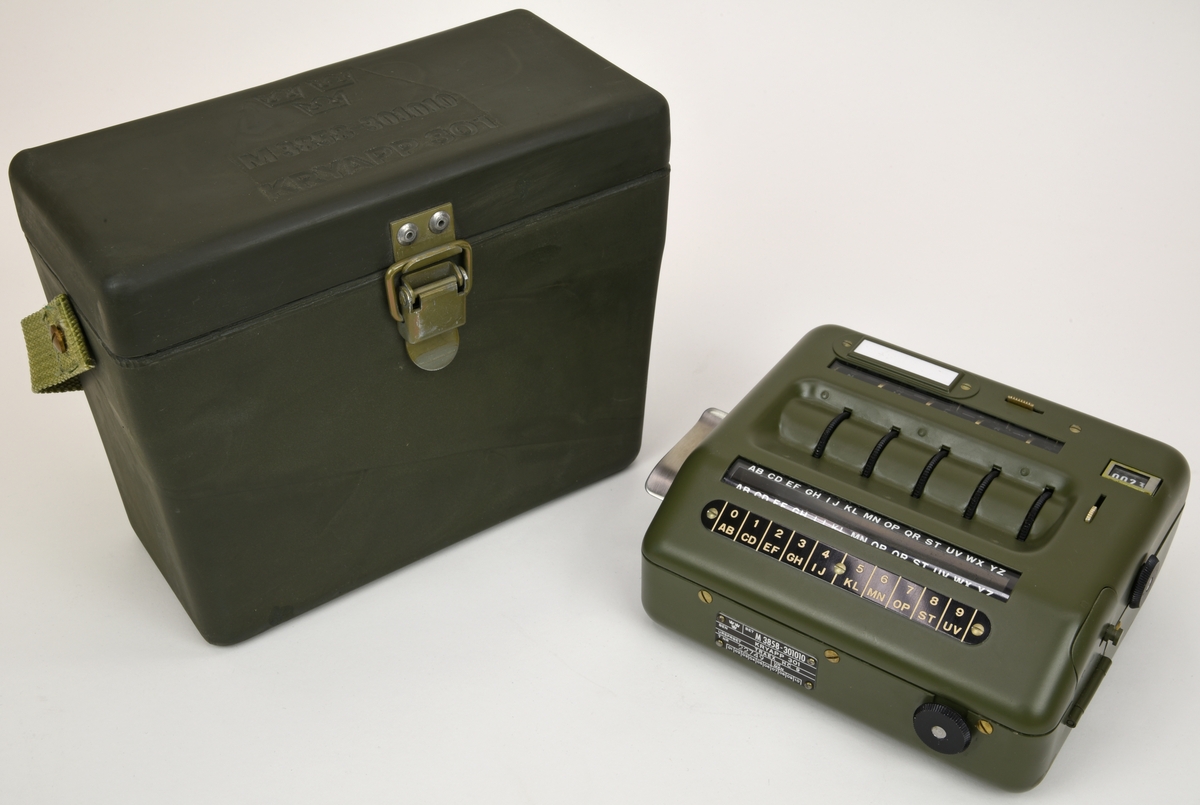 Krypteringsapparat (:1) med hölje av grönmålat aluminium i rundade former. Översidans framkant är lätt fasad och har ett avlångt fönster med alfabetet i över- och nederkant. Fönstret är till för att visa den alfabetsrulle som gav lösningen på kryptot. Under fönstret finns en svart skylt med vit text där siffrors bokstavskoder visas. På ovansidans mitt finns fem smala chifferhjul av svart bakelit i en försänkning. Hjulen är till för att ställa in chiffrets bokstäver som syns i ett fönster längst upp på apparatens ovansida. Till höger om chifferfönstret finns ett räkneverk med fyra siffror.

På apparatens framkant finns en skylt med M-nummer, serienummer och liknande och till höger ett vred av svart bakelit för att mata fram alfabetsrullen. På apparatens vänstra sida finns ett frammatningsvred av metall samt tillverkarens logotyp. På den högra sidan finns en lucka för alfabetsrullen och ett vred av bakelit för att ställa in chifferhjulaxeln. Baksidan har en större lucka för hålkortsplatsen och undersidan har små gummifötter samt en dekal med information om garantitid.

Till apparaten hör också en transportväska (:2) av formgjuten och genomfärgad gummi. Väskan är grön och har en vävd bärrem fäst med mässingsskruv. Locket är fäst med ett avlångt, nitat gångjärn och har ett låsspänne i mässing. På locket finns tre kronor och apparatens M-nummer i relief och på väskans undersida finns väskans M-nummer. Insidan av väskan är formad efter kryptoapparaten för att ge så mycket skydd som möjligt.

M-nummer: M 3858-301010
Tillverkningsnummer: 22749

Väskans M-nummer: M 7038-045010