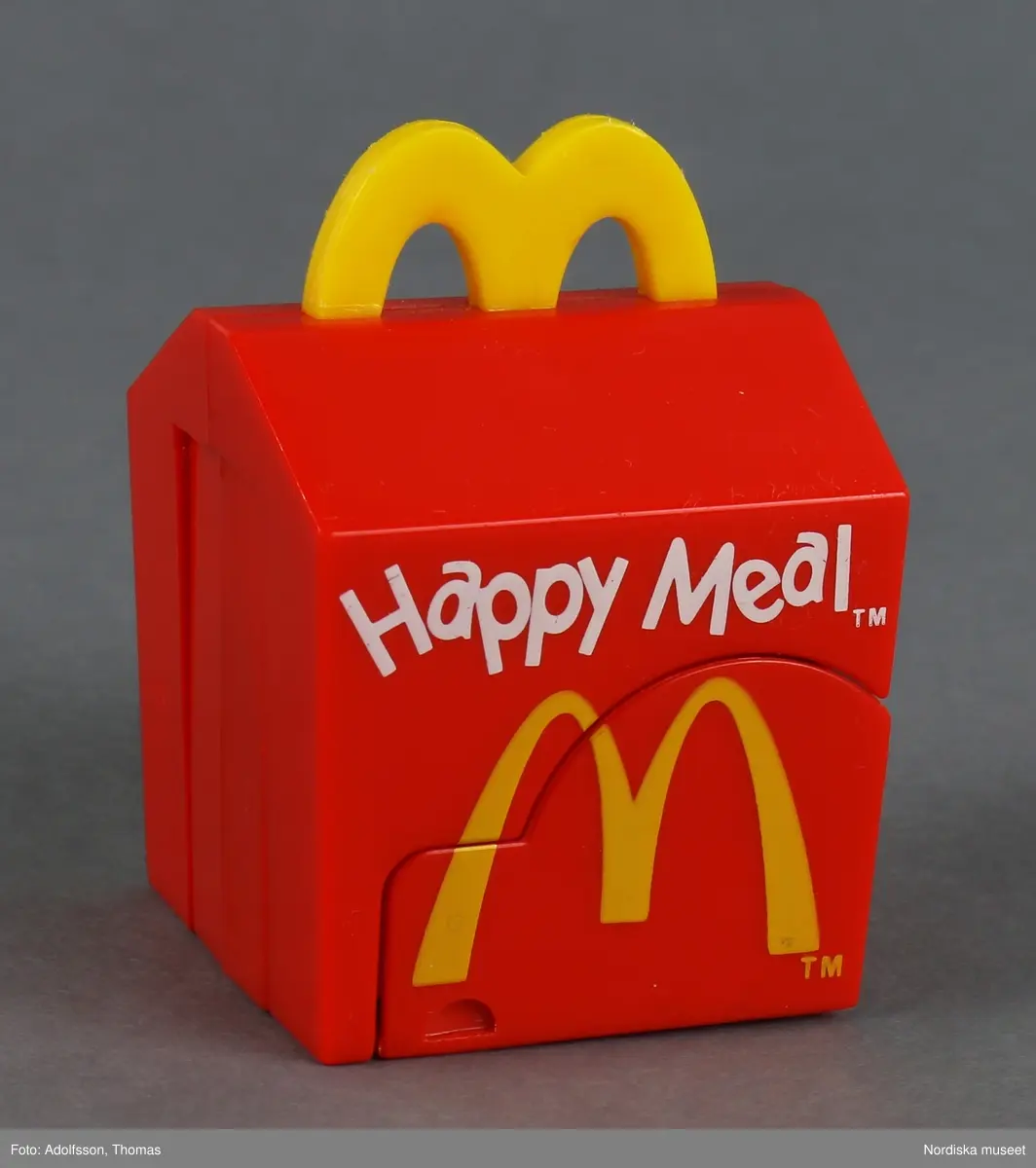 Leksak i form av en röd matkartong för hamburgare. På utsidan finns texten "Happy Meal" och symbolen M som står för matkedjan McDonald's. Sidorna går att fälla ut, varvid en djurfigur med huvud och tassar framträder.