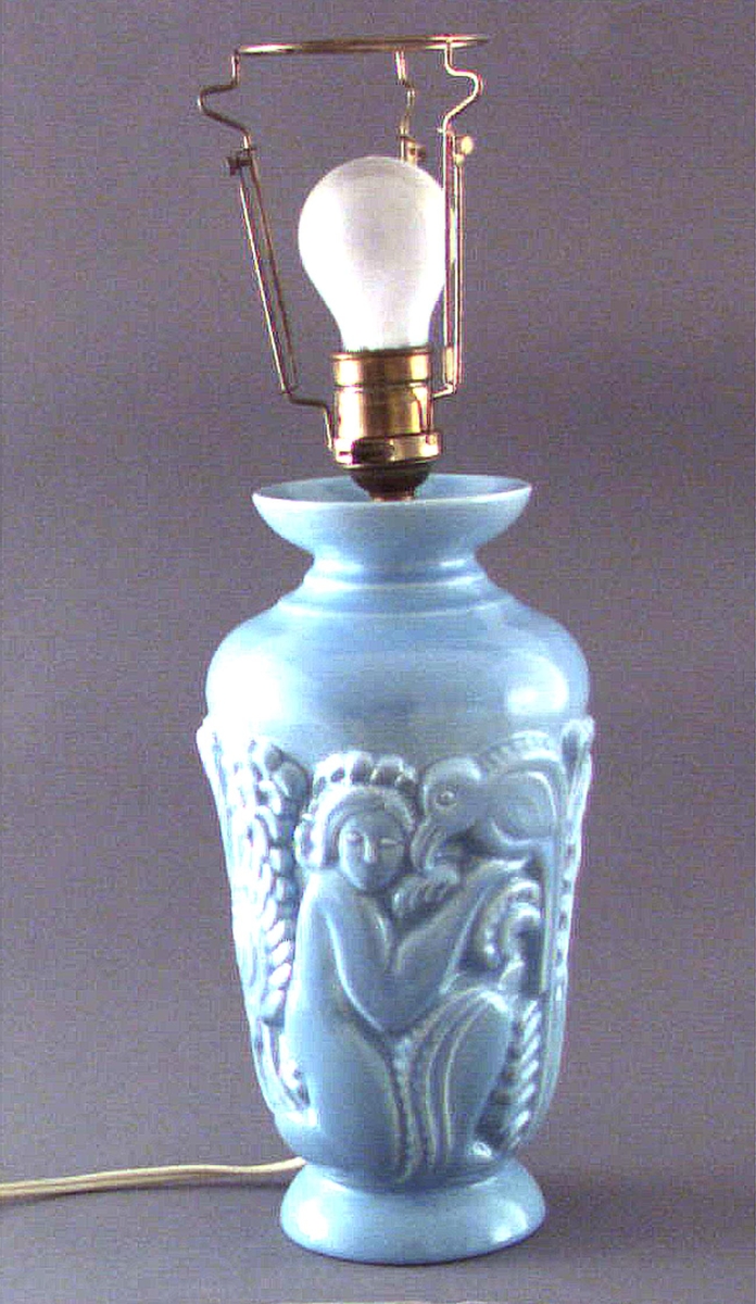 Lampfot. Formpressat motiv i form av människor och fåglar. Turkos glasyr. Signerad i sidan: RE (Ruben Wallström) samt i botten: RW A. Saknar fabriksstämplar. Saknar skärm men har elkabel samt glödlamphållare.