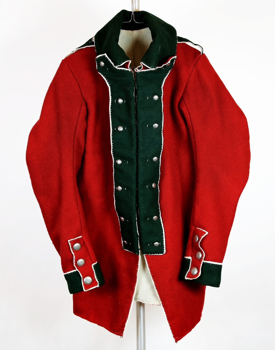 Jakke/kjole M1789 for Oplandske Infanteriregiment. Rekonstruert. Materialer: ullklede i krapprødt, mørkegrønt og hvitt. Fôrstoff: bay av ull. Knapper av tinn. Oplandske IRs kjenningsfarger var mørkegrønt med hvite passepoiler (kanter) og knapper i hvitt metall. Kjolen var i sin opprinelige form basert på en uniformsmodell innført i Russland noen år tidligere, der etter polsk forbilde. Russland var frem til 1807 Danmark-Norges viktigste alliansepartner mot Sverige. Snittet og passformen ble regnet som svært moderne og praktisk.