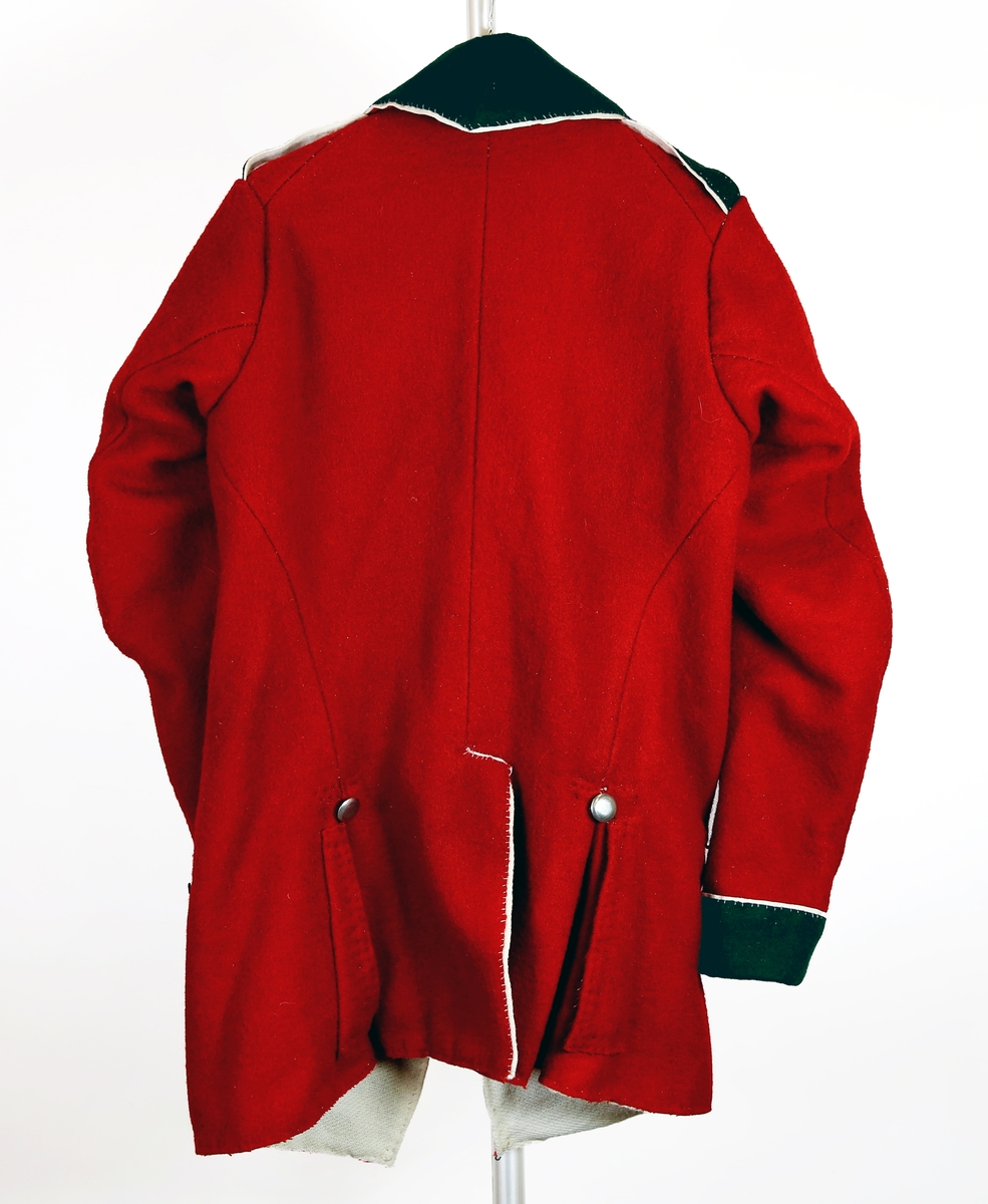 Jakke/kjole M1789 for Oplandske Infanteriregiment. Rekonstruert. Materialer: ullklede i krapprødt, mørkegrønt og hvitt. Fôrstoff: bay av ull. Knapper av tinn. Oplandske IRs kjenningsfarger var mørkegrønt med hvite passepoiler (kanter) og knapper i hvitt metall. Kjolen var i sin opprinelige form basert på en uniformsmodell innført i Russland noen år tidligere, der etter polsk forbilde. Russland var frem til 1807 Danmark-Norges viktigste alliansepartner mot Sverige. Snittet og passformen ble regnet som svært moderne og praktisk.