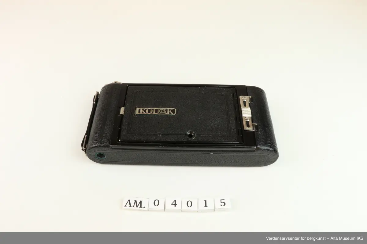 Foldet fotoapparat Diomatic NO. 1A Pocket Kodak. Made in U.S.A by Eastman Kodak Company. Rochester. N.Y.
Kodak Anastigmat F 6.3-12.7mm lens NO. 18339.
Kamera med rektangulær form og avrundede sider. 
På undersiden et hull med gjenger der noe kan skrus inn.
På oversiden metalldel med en nøkkellignende utsikker som kan vris rundt.
Metallås. Firkantet luke på baksiden for kameralinsen, og rundt rødt vindu til bildetelling.
Åpnes ved å dra ned metallås.
Kameraet kommer i et brunt lærveske med 530mm lang stropp.