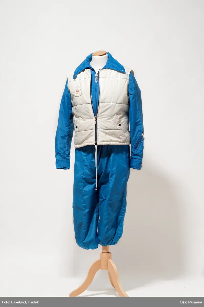 Dameskidress i tre deler. A: Kort jakke og B: Bukse med vide ben og seler. Begge deler i blått boblestoff av polypropylen i størrelse 42. C: Vest i kremhvit farge i samme stoff og størrelse.