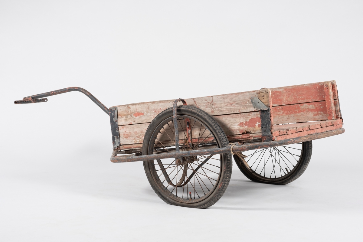 Tralle på to gummihjul. Rektangulær kasse dannet av liggende plank, en manglende kant på kortende. Metallforsterkning på alle hjørner. Understell dannet av  bøyde jernrør, hvor ett danner håndtaket. Tverrliggende jernrør til håndtering.