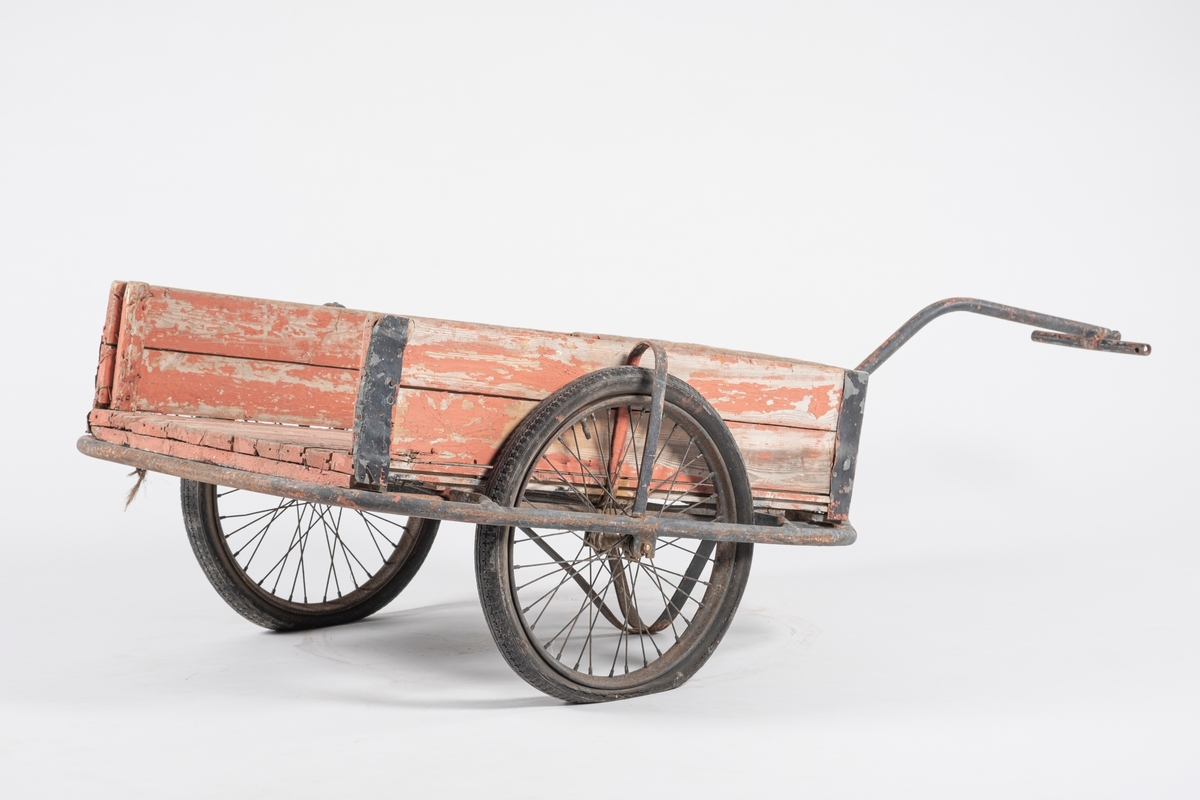 Tralle på to gummihjul. Rektangulær kasse dannet av liggende plank, en manglende kant på kortende. Metallforsterkning på alle hjørner. Understell dannet av  bøyde jernrør, hvor ett danner håndtaket. Tverrliggende jernrør til håndtering.