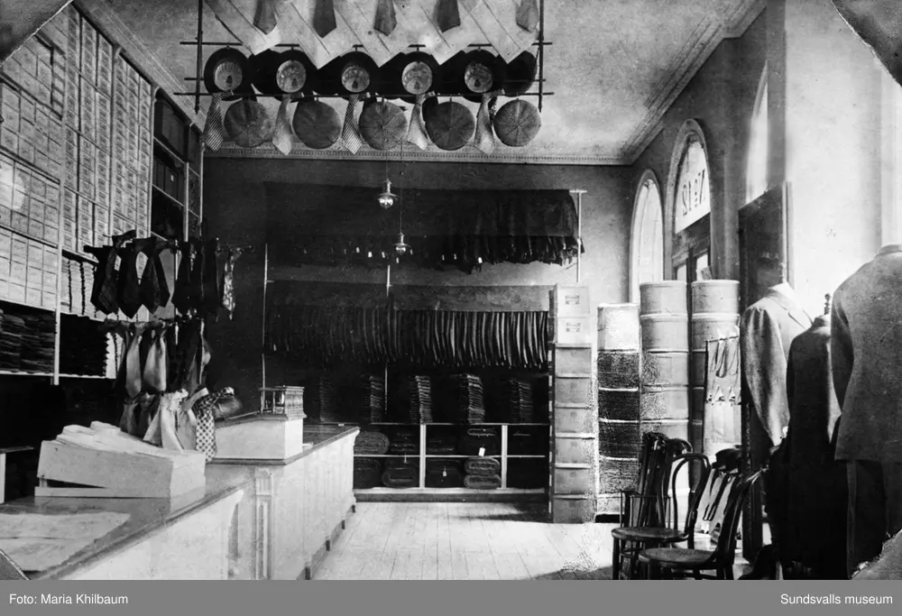 Rosenbaums herrekiperingsaffär. Interiörer. Ur album med skinnpärmar märkt "A. R. 1886 27/12 1936". A. R. står för Albert Rosenbaum (f. 1886 d. 1950) som var butikschef och tillika son till grosshandlaren Salomon Rosenbaum (f. 1849 d. 1910) som grundade klädfirman. Den första bilden är märkt "Första ombyggnaden" och är troligen tagen 1907 då man flyttade till Sjögatn 12 (man hade tidigare från 1897 en butik på Storgatan). Den andra bilden är märkt "Andra ombyggnaden" och kan vara tagen på 1920-talet. Den tredje och fjärde bilden är märkt "Tredje ombyggnaden" och är tagen 1936 av Maria Kihlbaum. Resterande bilder är ej daterade.