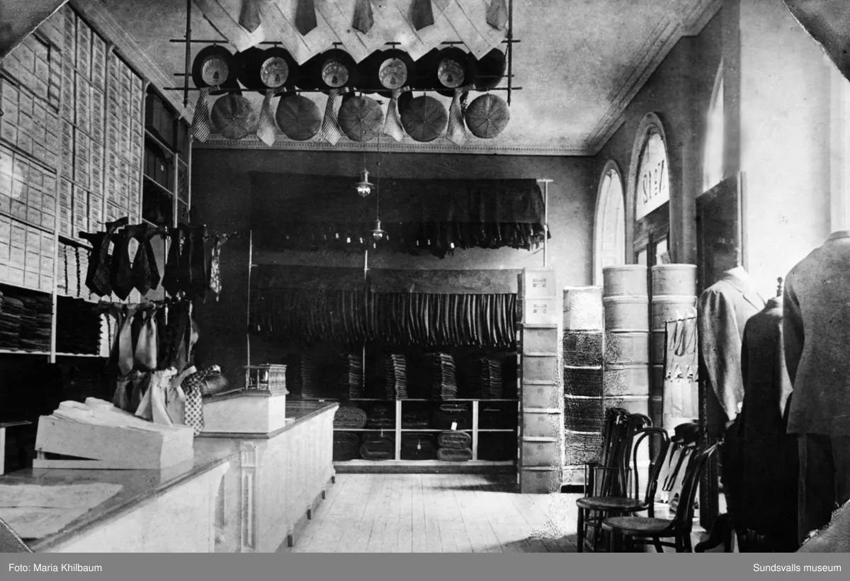 Rosenbaums herrekiperingsaffär. Interiörer. Ur album med skinnpärmar märkt "A. R. 1886 27/12 1936". A. R. står för Albert Rosenbaum (f. 1886 d. 1950) som var butikschef och tillika son till grosshandlaren Salomon Rosenbaum (f. 1849 d. 1910) som grundade klädfirman. Den första bilden är märkt "Första ombyggnaden" och är troligen tagen 1907 då man flyttade till Sjögatn 12 (man hade tidigare från 1897 en butik på Storgatan). Den andra bilden är märkt "Andra ombyggnaden" och kan vara tagen på 1920-talet. Den tredje och fjärde bilden är märkt "Tredje ombyggnaden" och är tagen 1936 av Maria Kihlbaum. Resterande bilder är ej daterade.