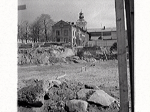 Fastigheten kv Trädgården 6, Varberg. Grundschaktning för Domusbygget är klart. Artikel i samband med bilden publicerad i Varbergs Tidning 1962-05-07.
Fotot visar den urschaktade marken och omgivningarna. Fastigheterna i bakgrunden är Läkaren 9, (Varbergs stadshotell), Rappeska huset (revs 1969?) och en del av Brunnsparken 5.
