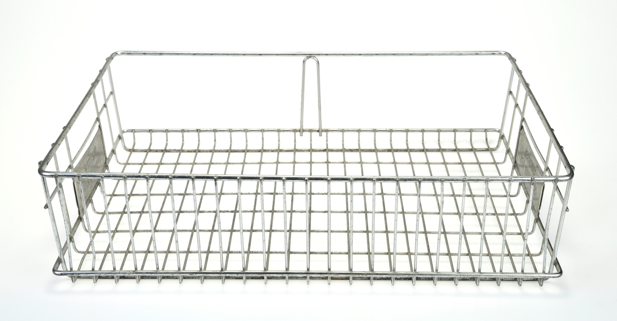 To identiske trådkurver av metall. Kurvene er firkantet med avrundede hjørner. I bunnne er rutene 2,5x5,0cm og i bakkant er de 2,5x13,0cm. På kortsidene er det ruter på sidene og et håndtak på midten. Under håndtakene er det montert på metallskilt med tekst, se "Påført tekst/merker". I front er kurvene åpne med unntak av en bøyle på midten. Kurvene er brukt på Konditor Erichsen, trolig til transport av bakst.