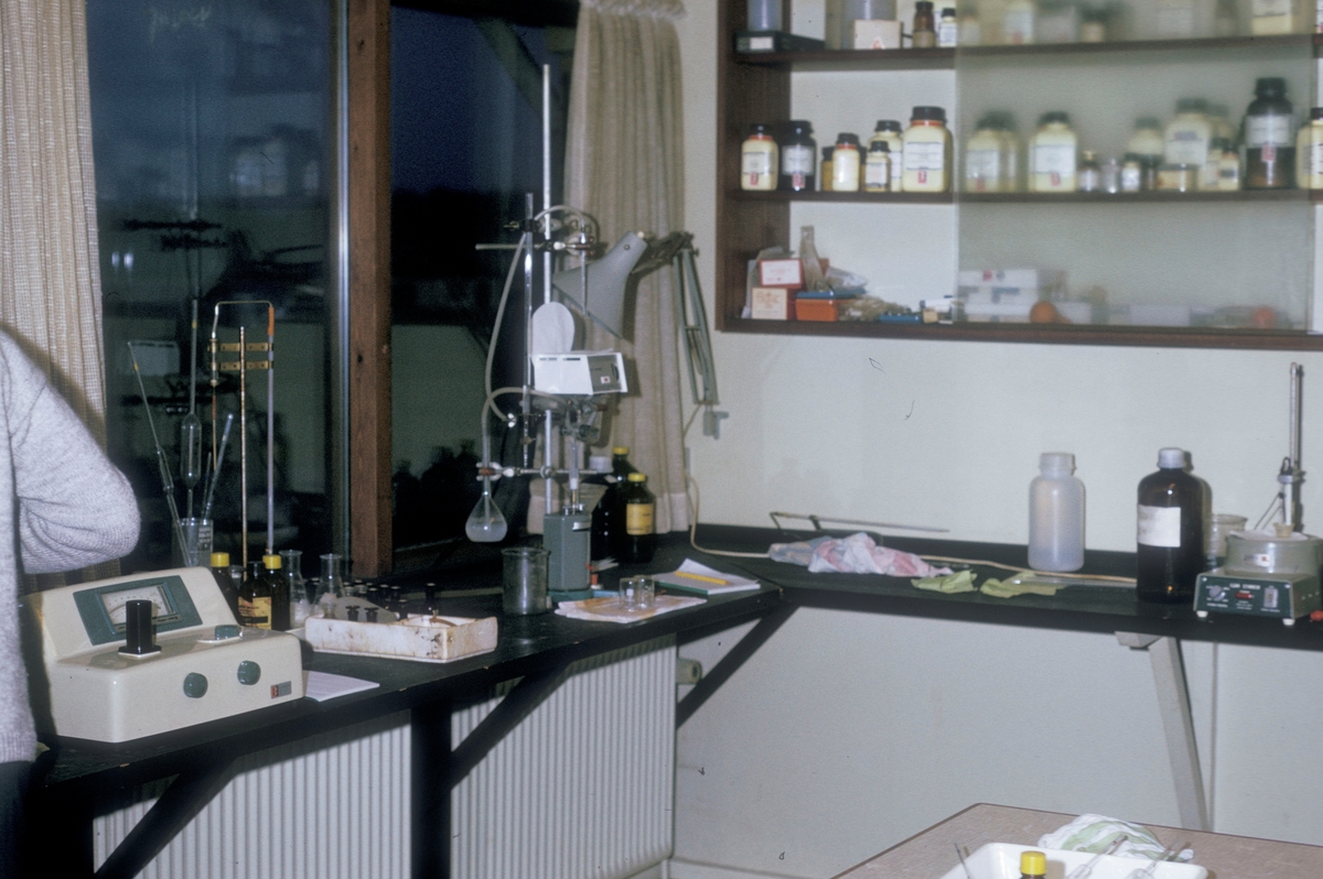 Forsøgsdambruget i Brøns, Danmark, 1974 : Et laboratorium med diverse apparater og instrumenter på arbeidsbenken og krukker og glass i en hylle på veggen.