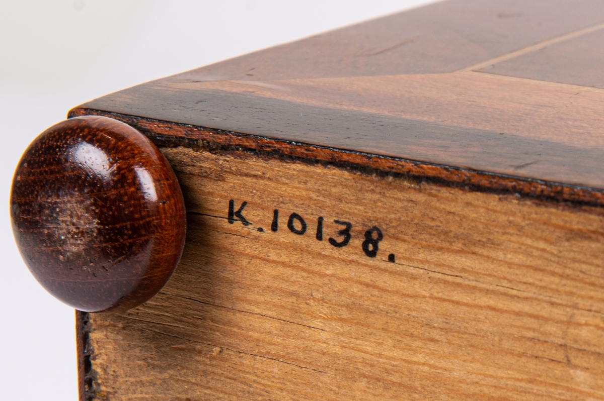 Kat.kort:
Syskrin, mahogny, på låga kulfötter, inlagd oval figur på locket. Nyckelskylt av ben.