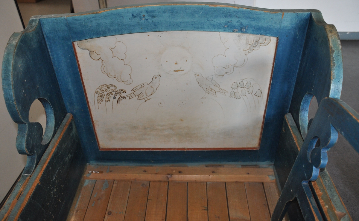 Uttrekkbar barneseng av tre, i to deler. Sengen er malt blå med dekorative røde linjer ved kanter. Hode- og endegavel har kurvet form øverst, og fylling på utsiden. Det er malt dekor på utsiden av endegavel og sideplater, og på innsiden av hodegavel. Motiv på maling av to fugler og sol på hodegavel, to trær og Sør-Fron kirke på endegavel og kuer og trær på sidegavler. Spesielt på hodegavel er malingen avlitt. Det følger med en løs sengehest med sveifet dekor.