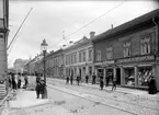 Östra Storgatan åt öster från Borgmästargränd I Jönköping. Murningsarbete pågår i fastighet nr: 5. I husen finns olika affärer, till exempel musikhandel, cigarraffär, klädaffärer och en kaffehandel.