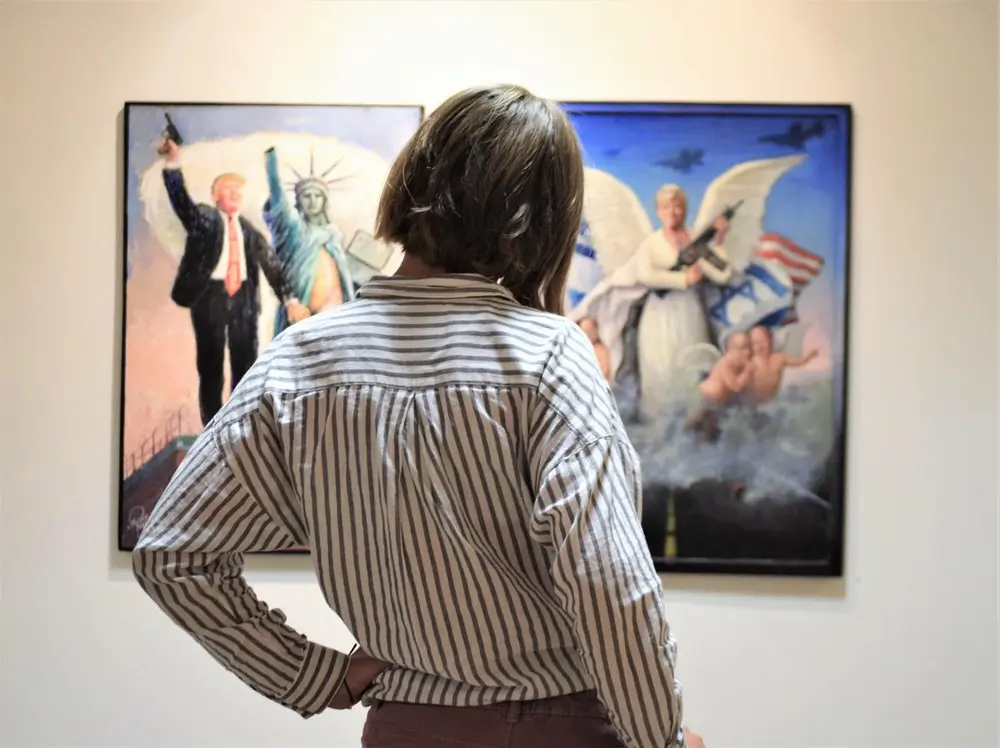 Ung jente ser på to tegninger som henger på veggen i et galleri.