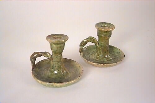 Handdrejad ljusstake av lergods, typ kontorsljusstake. Ljushållare för ett ljus på rund fotplatta med vriden grepe. Ljusgrön bottenlasyr med gröna och bruna sänk. Fotplattan är sprucken tvärs över. På undersidan oläslig text.