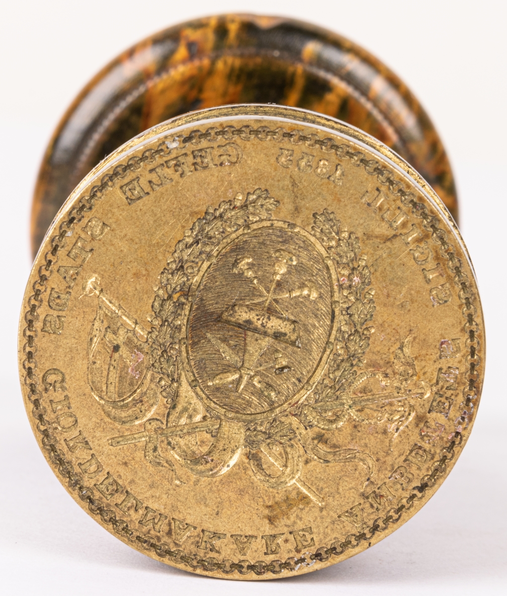 Gefle stads giördelmakareämbetes sigill, 1833. Fodral av sämskinn.

Lappkort.
Sigill, stamp av mässing, svarvat träskaft, av gröngul färg. Geflestads stads gördelmakare ämbets sigill 1833.