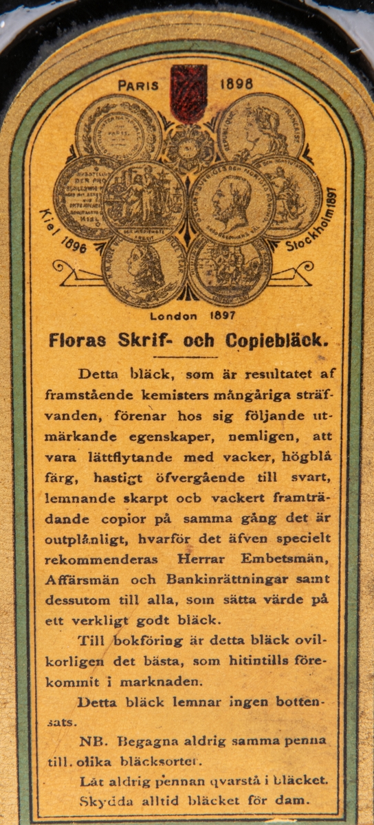 Bläckflaska med innehåll. Av glas. Oöppnad. Etiketter på samtliga sidor, varav framsidans i rött och med texten "FLORAS SKRIF & COPIEBLECK - TEKNISKA AKTIEBOLAGET FLORA I GEFLE", m.m.
Kvadratisk genomskärning med fasade hörn. Rundas upp till en smal rund hals med horisontell krage överst. Förseglad med pappetikett över korken. Etiketter på samtliga sidor, varav framsidans i rött med detaljer i flera färger. Sidoetiketterna har längre beskrivningar av bläcket på svenska resp. franska. På baksidan räknas prisbelöningar upp.