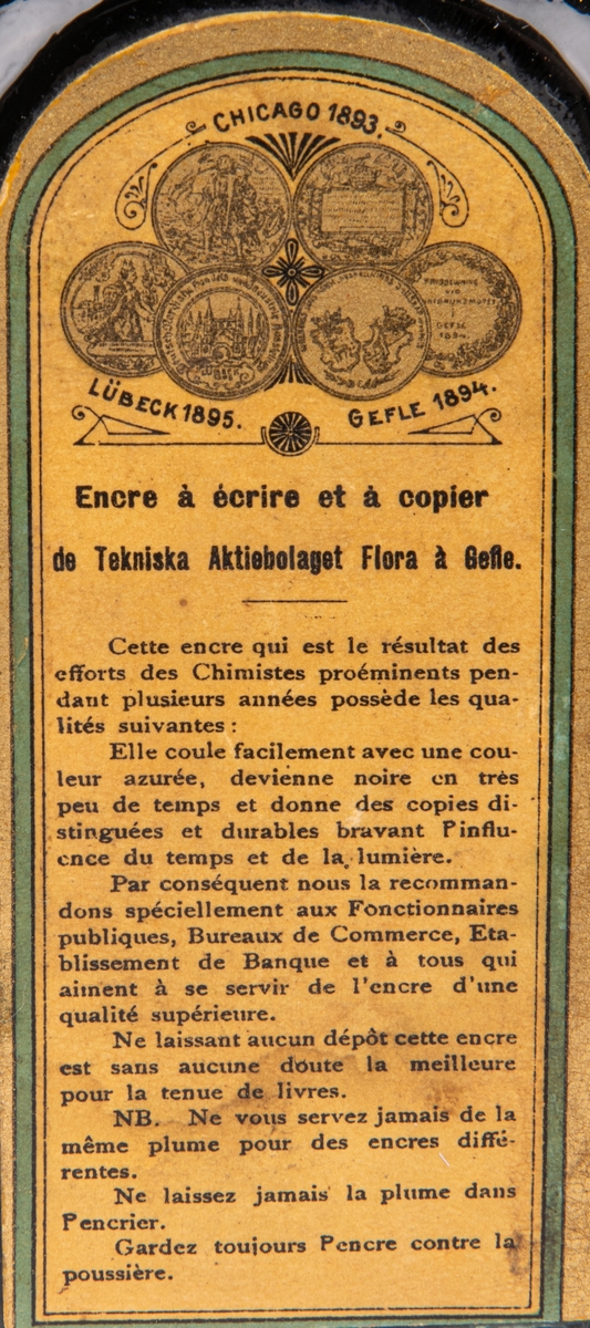 Bläckflaska med innehåll. Av glas. Oöppnad. Etiketter på samtliga sidor, varav framsidans i rött och med texten "FLORAS SKRIF & COPIEBLECK - TEKNISKA AKTIEBOLAGET FLORA I GEFLE", m.m.
Kvadratisk genomskärning med fasade hörn. Rundas upp till en smal rund hals med horisontell krage överst. Förseglad med pappetikett över korken. Etiketter på samtliga sidor, varav framsidans i rött med detaljer i flera färger. Sidoetiketterna har längre beskrivningar av bläcket på svenska resp. franska. På baksidan räknas prisbelöningar upp.
